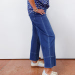 Person wearing a blue patterned top and blue jeans with white sneakers on a plain background