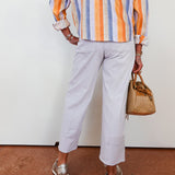 Person wearing a colorful striped shirt and light gray pants, holding a woven bag.