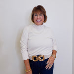 Woman wearing a white turtleneck sweater and blue jeans with a gold belt against a white background