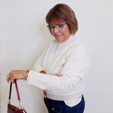 Woman in a white sweater and blue jeans holding a red handbag against a white wall.