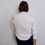 Person wearing a light gray sweater and dark pants against a white wall