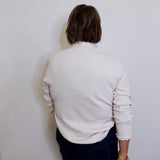 Person wearing a light gray sweater and dark pants against a white wall