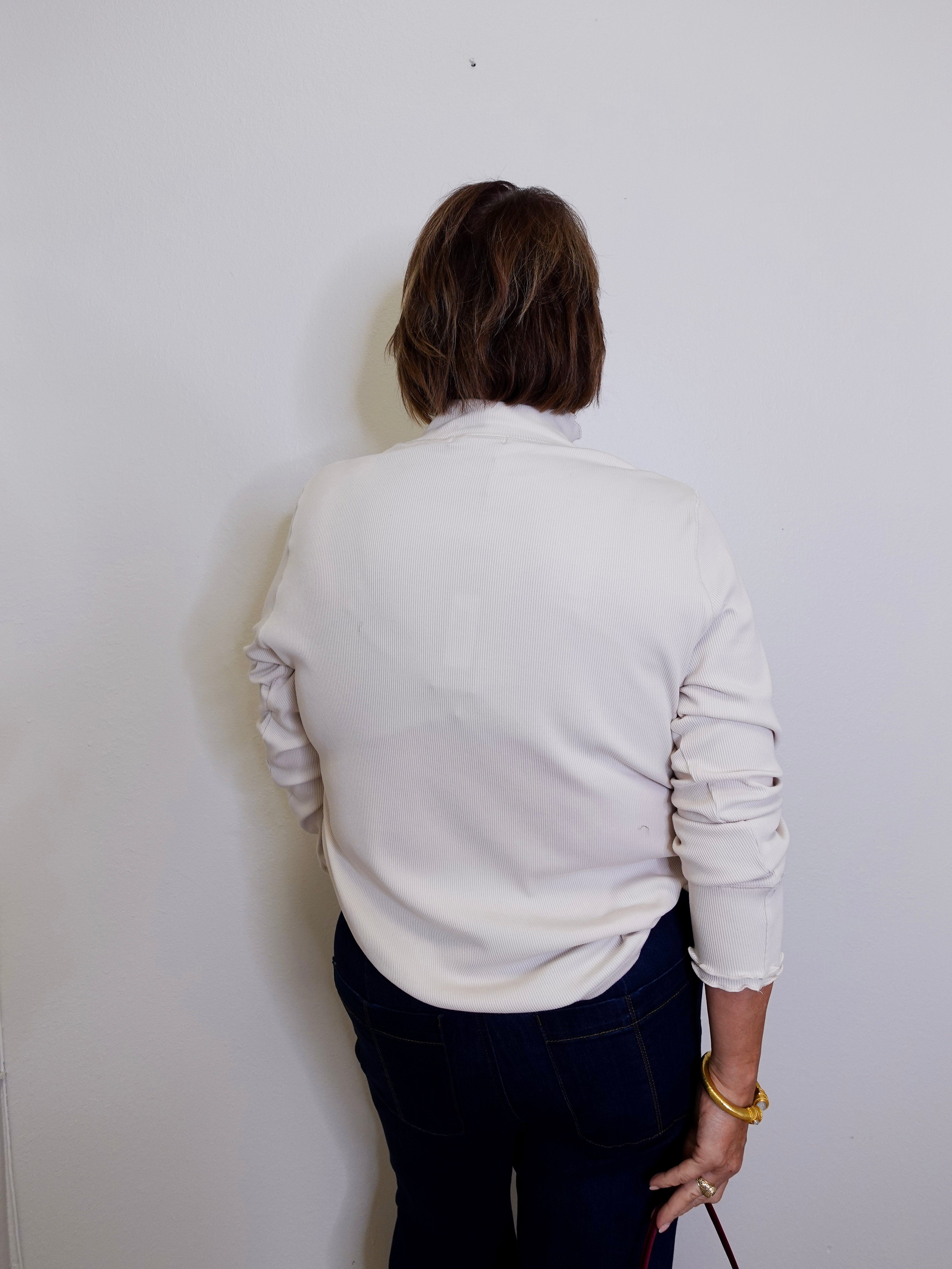 Person wearing a light gray sweater and dark pants against a white wall