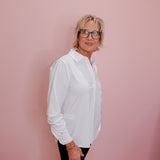 Person wearing a white shirt and black pants against a pink wall