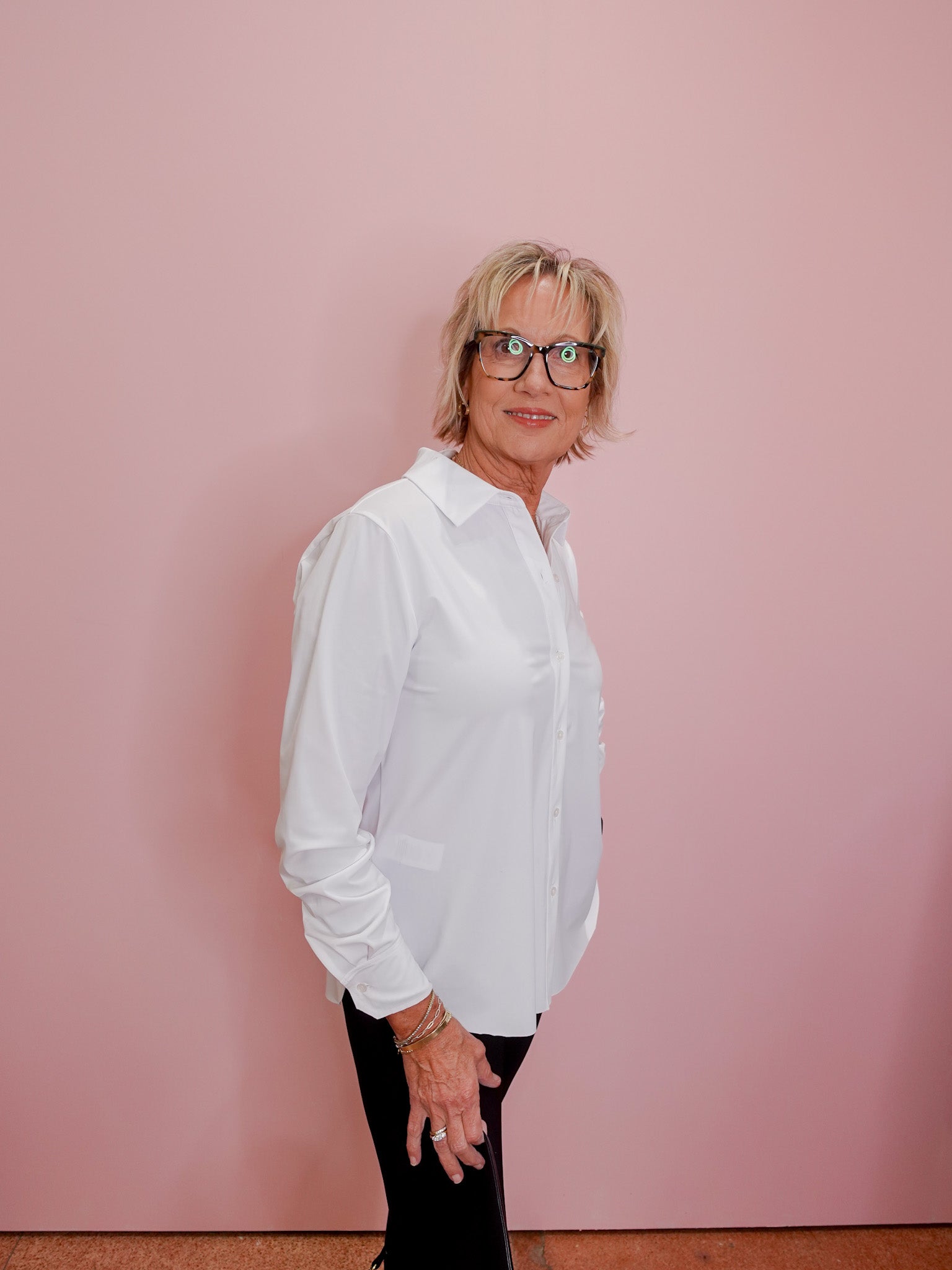 Person wearing a white shirt and black pants against a pink wall