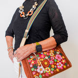 Woman holding a brown handbag with floral embroidery against a white background