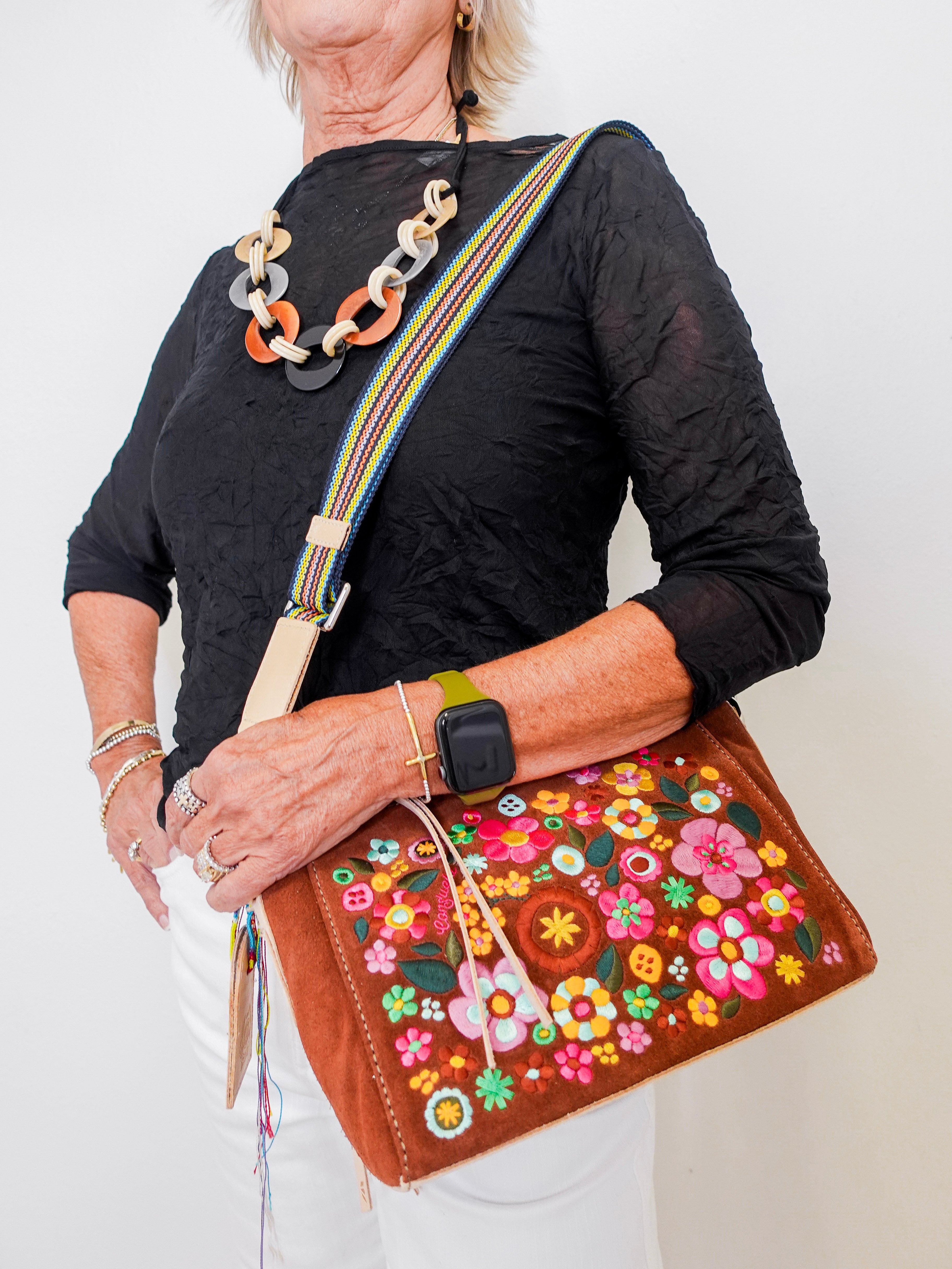 Woman holding a brown handbag with floral embroidery against a white background