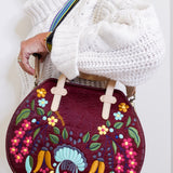Handbag with floral and rooster design held by a person wearing a white sweater.