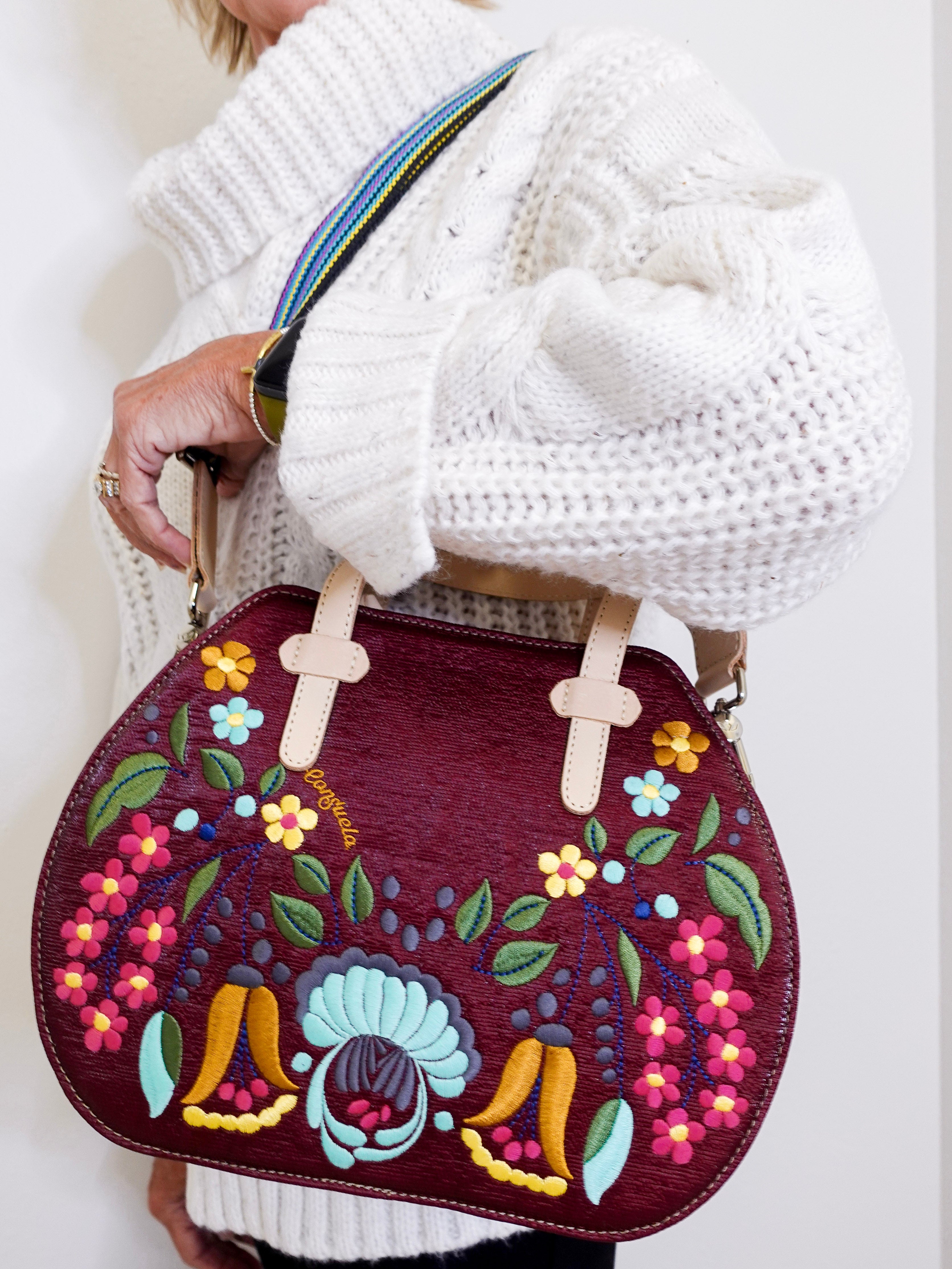 Handbag with floral and rooster design held by a person wearing a white sweater.