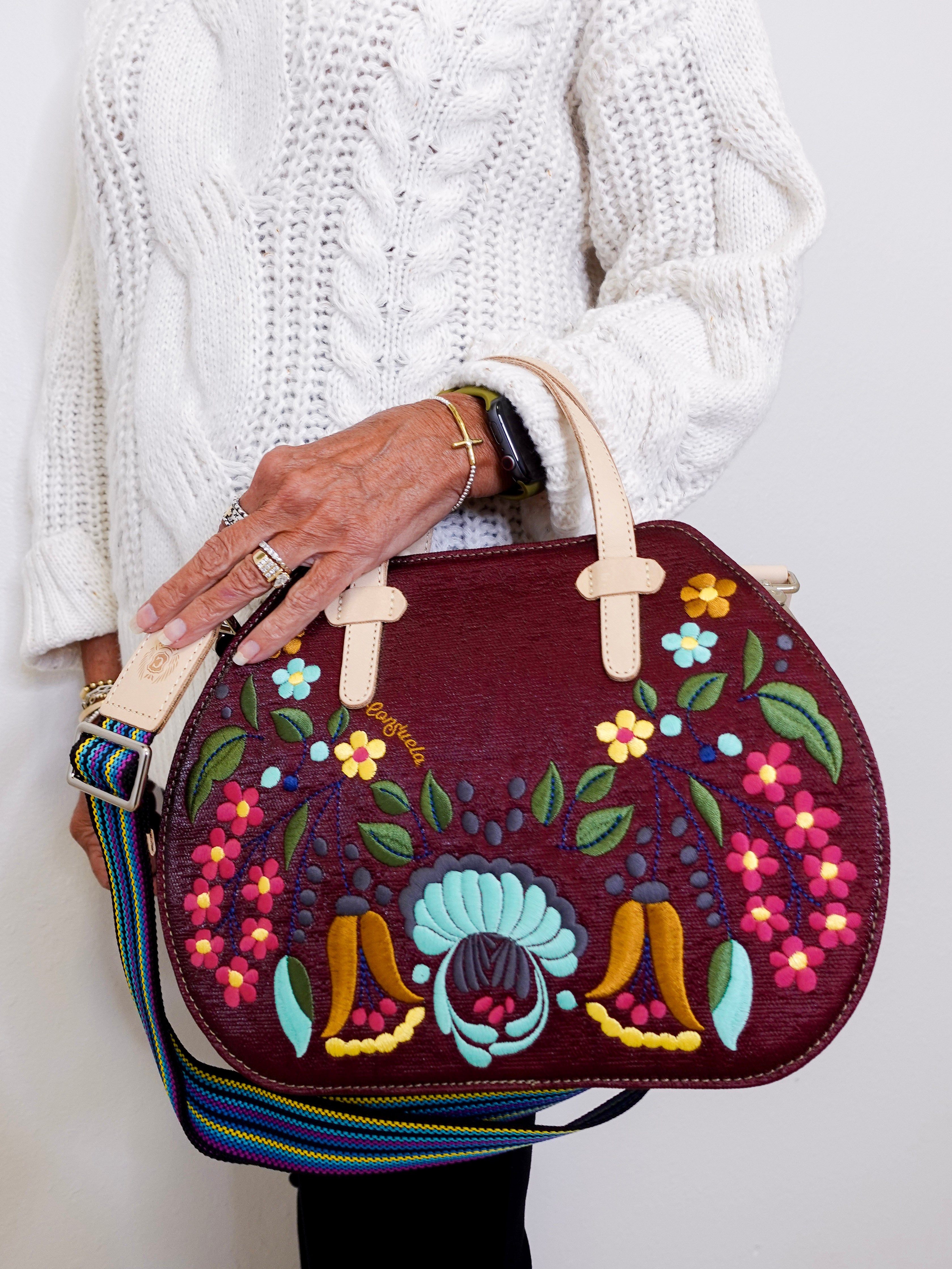 Person holding a colorful embroidered handbag against a white background