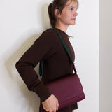 woman wearing consuela plum on the town crossbody-bag against a white background. 