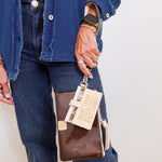 Person holding a brown leather wallet with a tag, wearing a blue jacket and jeans.
