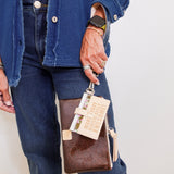 Person holding a brown leather wallet with a tag, wearing a blue jacket and jeans.
