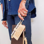 Person holding a brown wallet with a gold tag and tassel, wearing a blue denim jacket.