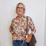 Person wearing a floral shirt and jeans, holding a brown bag against a white wall