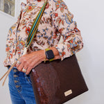 Person wearing a floral blouse and holding a brown leather bag against a white background