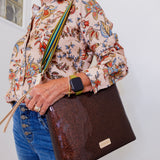 Person wearing a floral blouse and holding a brown leather bag against a white background