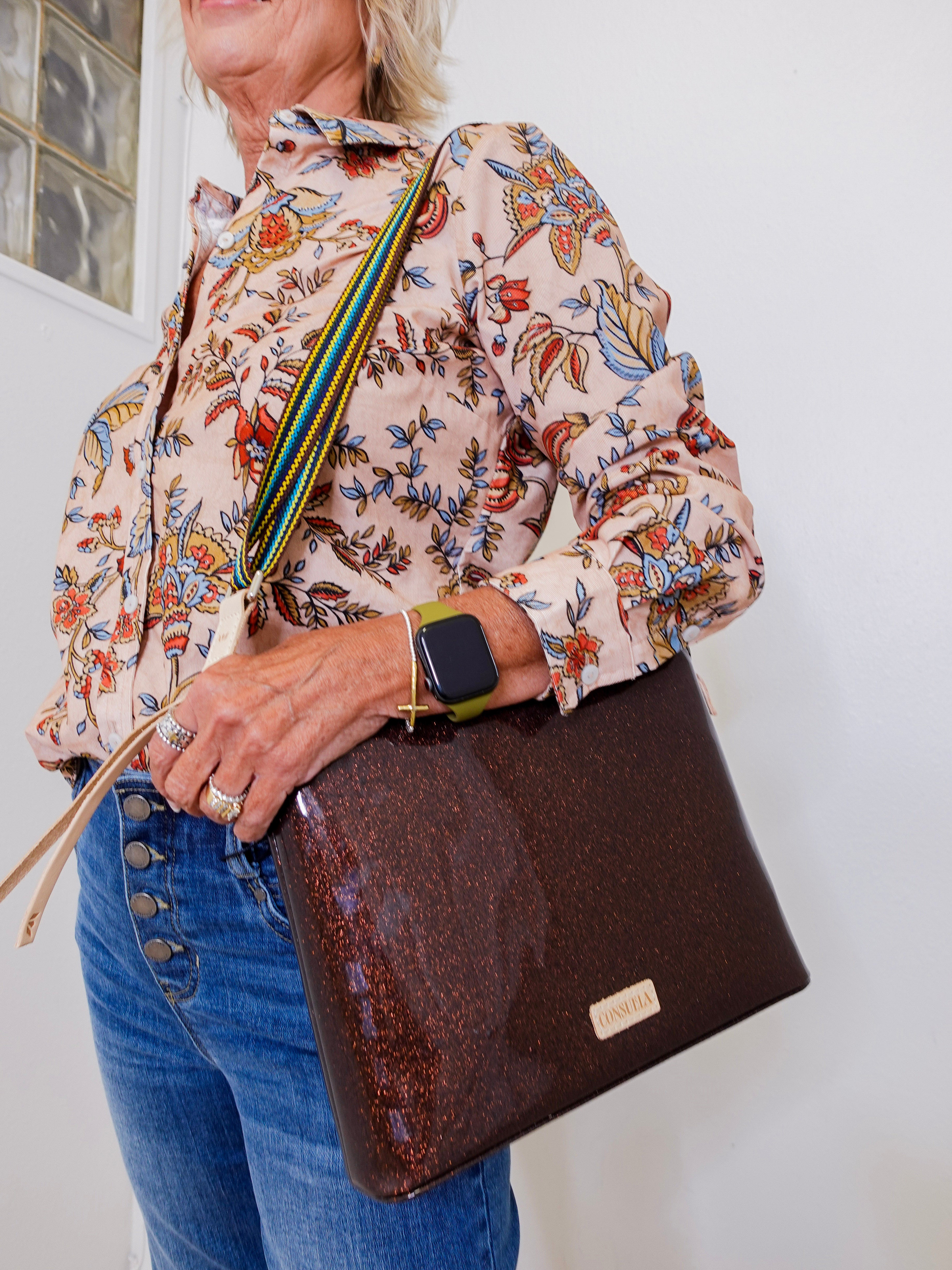 Person wearing a floral blouse and holding a brown leather bag against a white background
