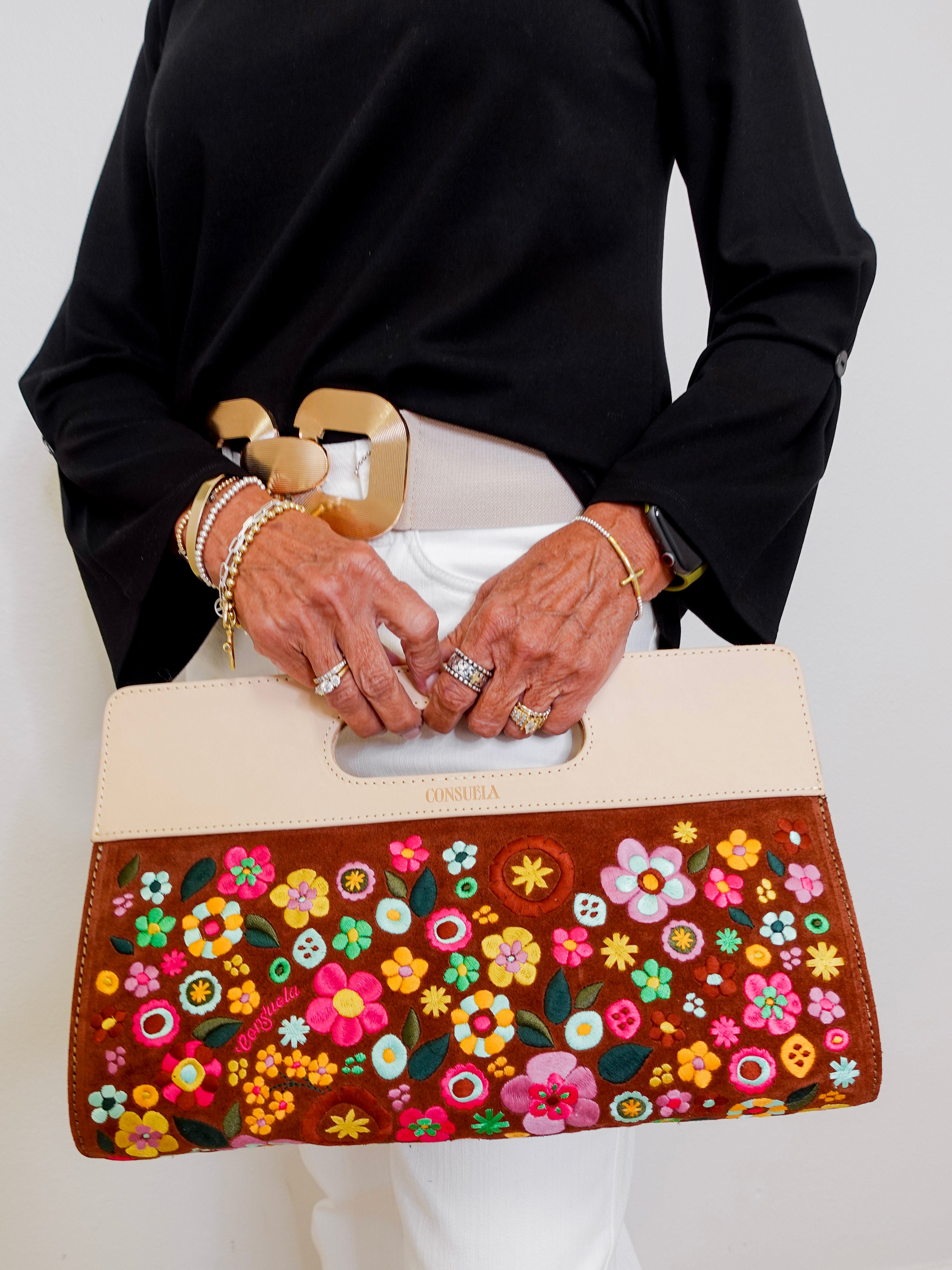 Person holding a handbag with floral design and gold accents