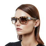 Woman wearing tortoiseshell sunglasses with a white background