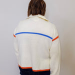 Person wearing a white sweater with colorful stripes on a plain background