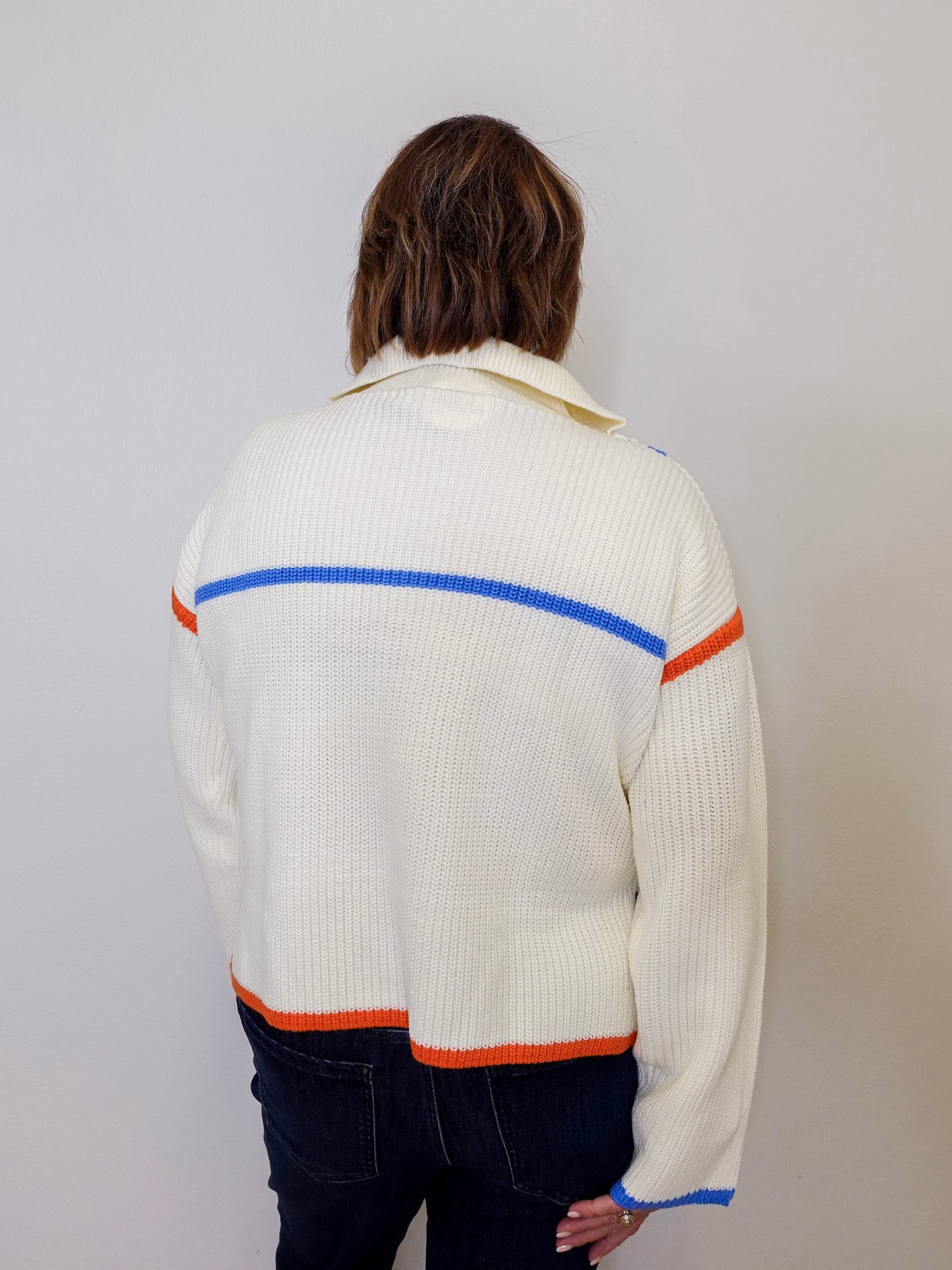 Person wearing a white sweater with colorful stripes on a plain background