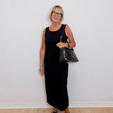Woman in a black dress holding a black handbag against a white wall.