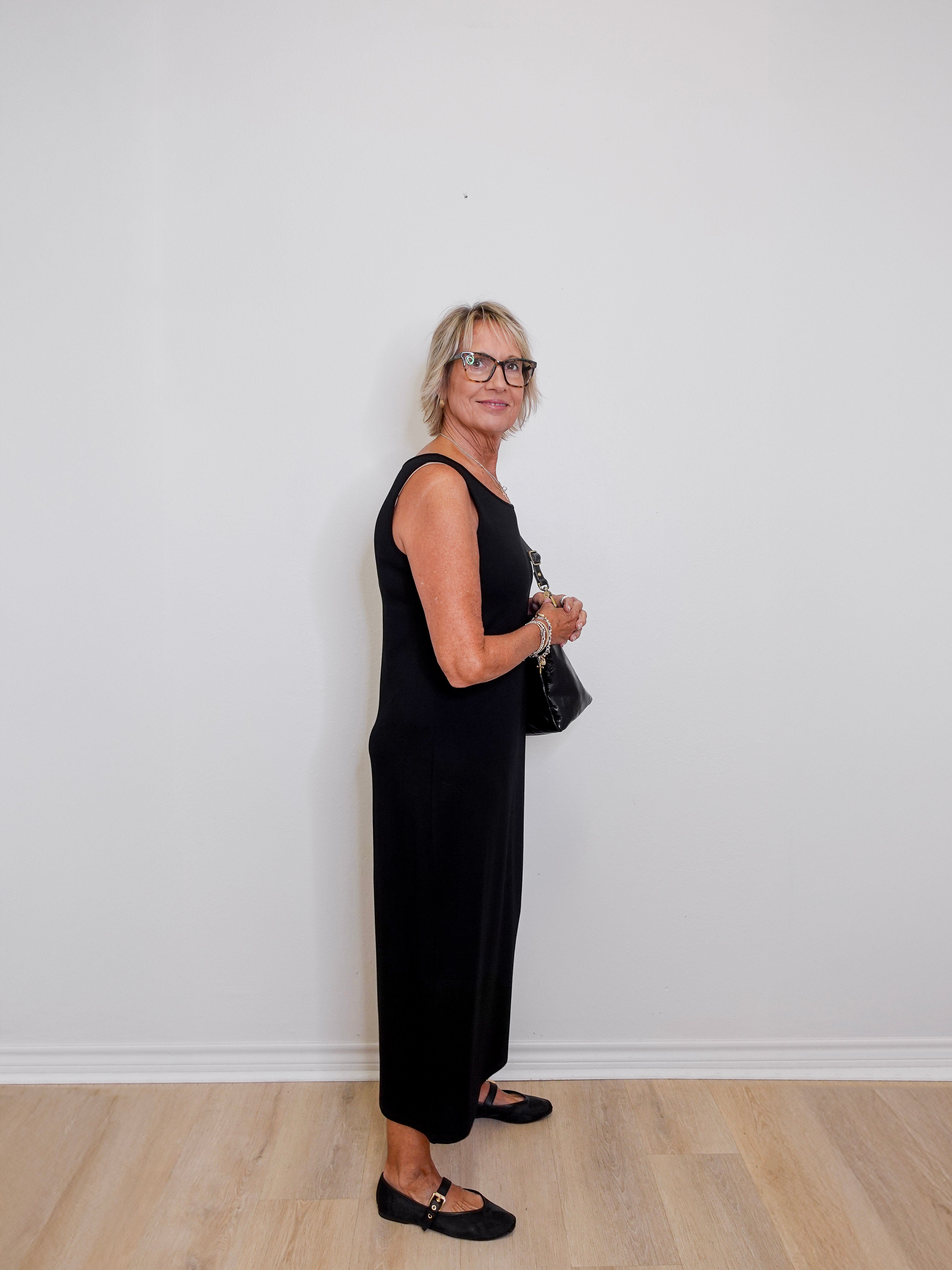 Woman in a black outfit standing against a white wall