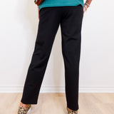 Person wearing black pants and leopard print shoes against a white wall.