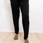 Person wearing black pants and leopard print shoes on a light wooden floor.