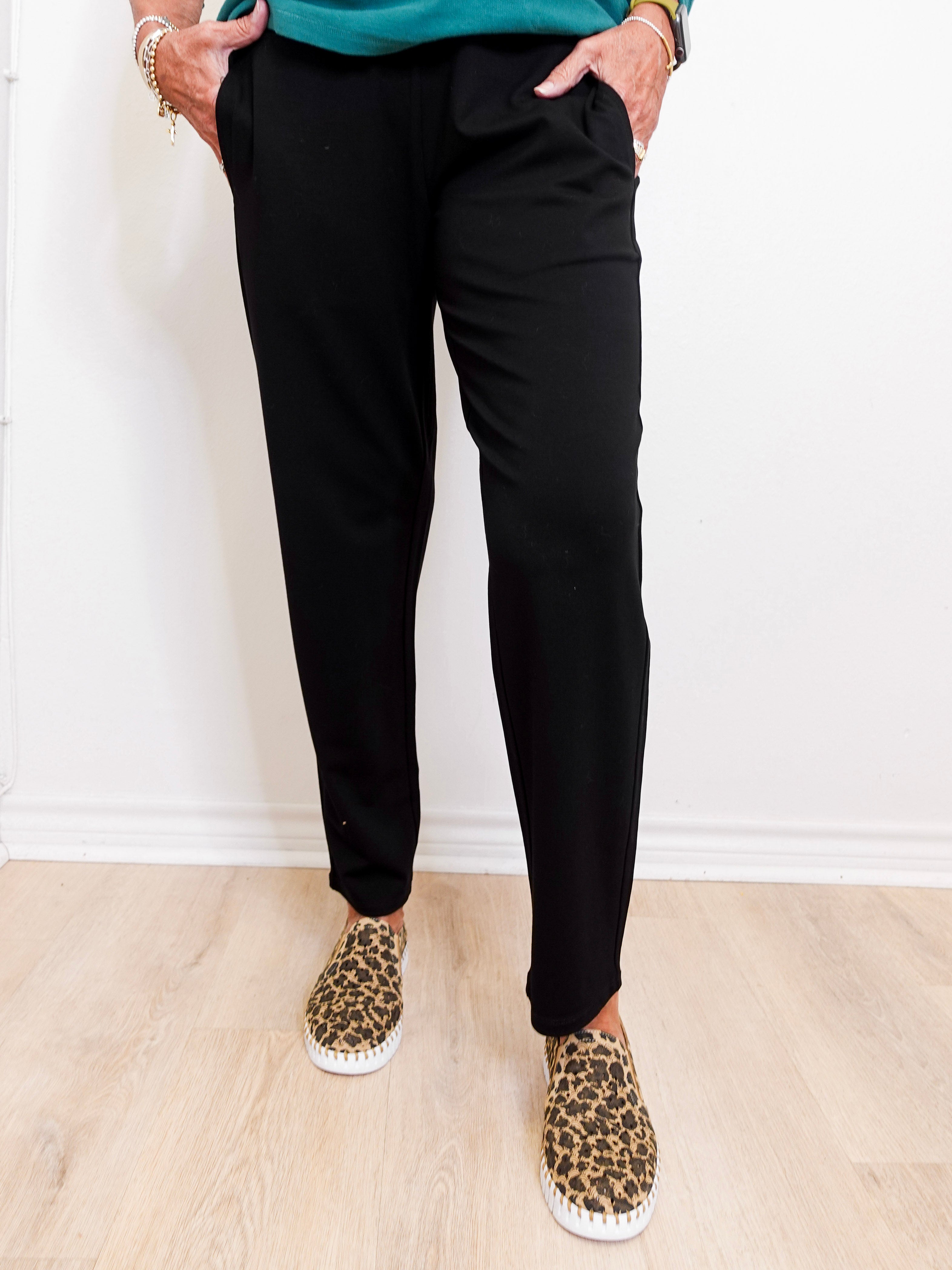 Person wearing black pants and leopard print shoes on a light wooden floor.