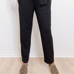 Person wearing black pants and leopard print shoes on a light wooden floor.