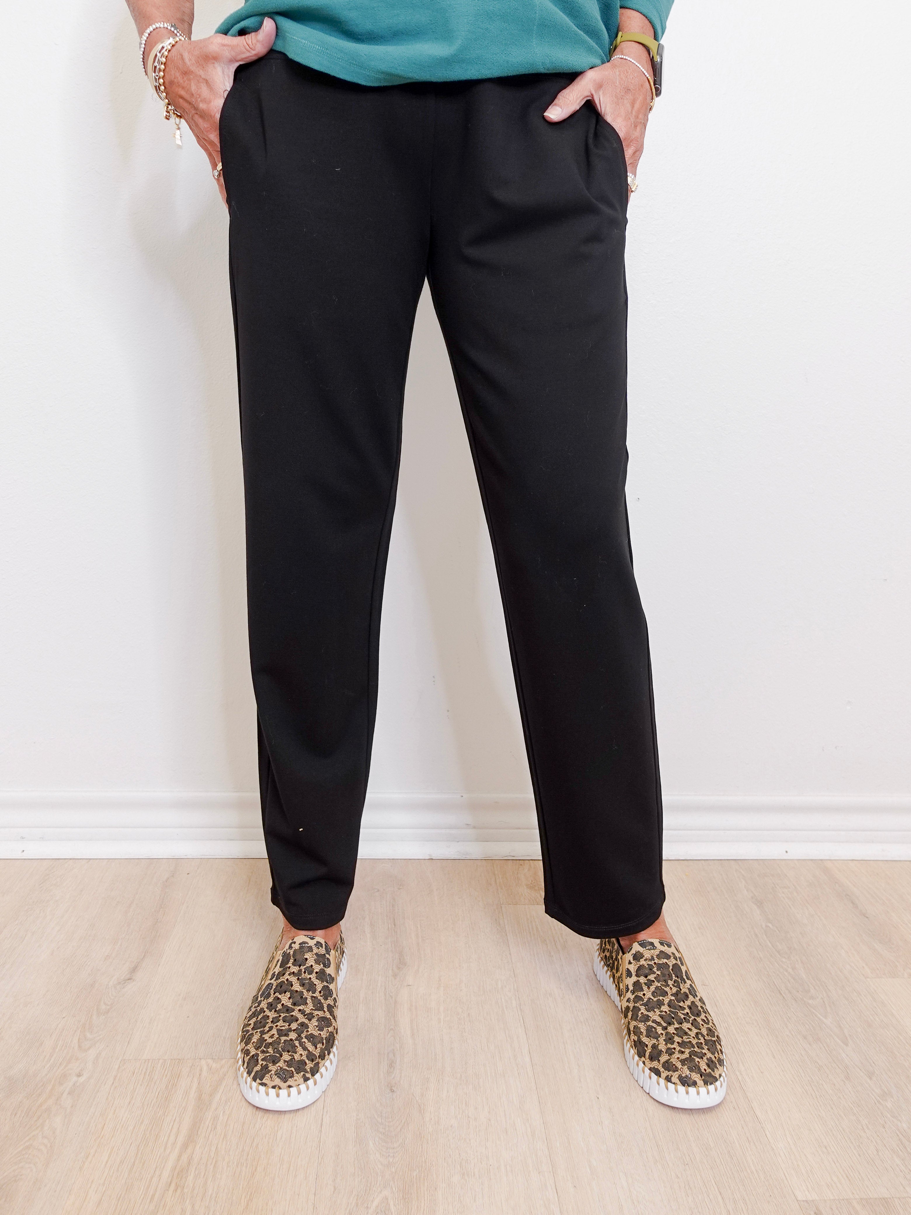 Person wearing black pants and leopard print shoes on a light wooden floor.