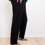 Person wearing black pants and leopard print shoes on a light wooden floor.