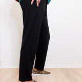 Person wearing black pants and leopard print shoes on a light wooden floor.