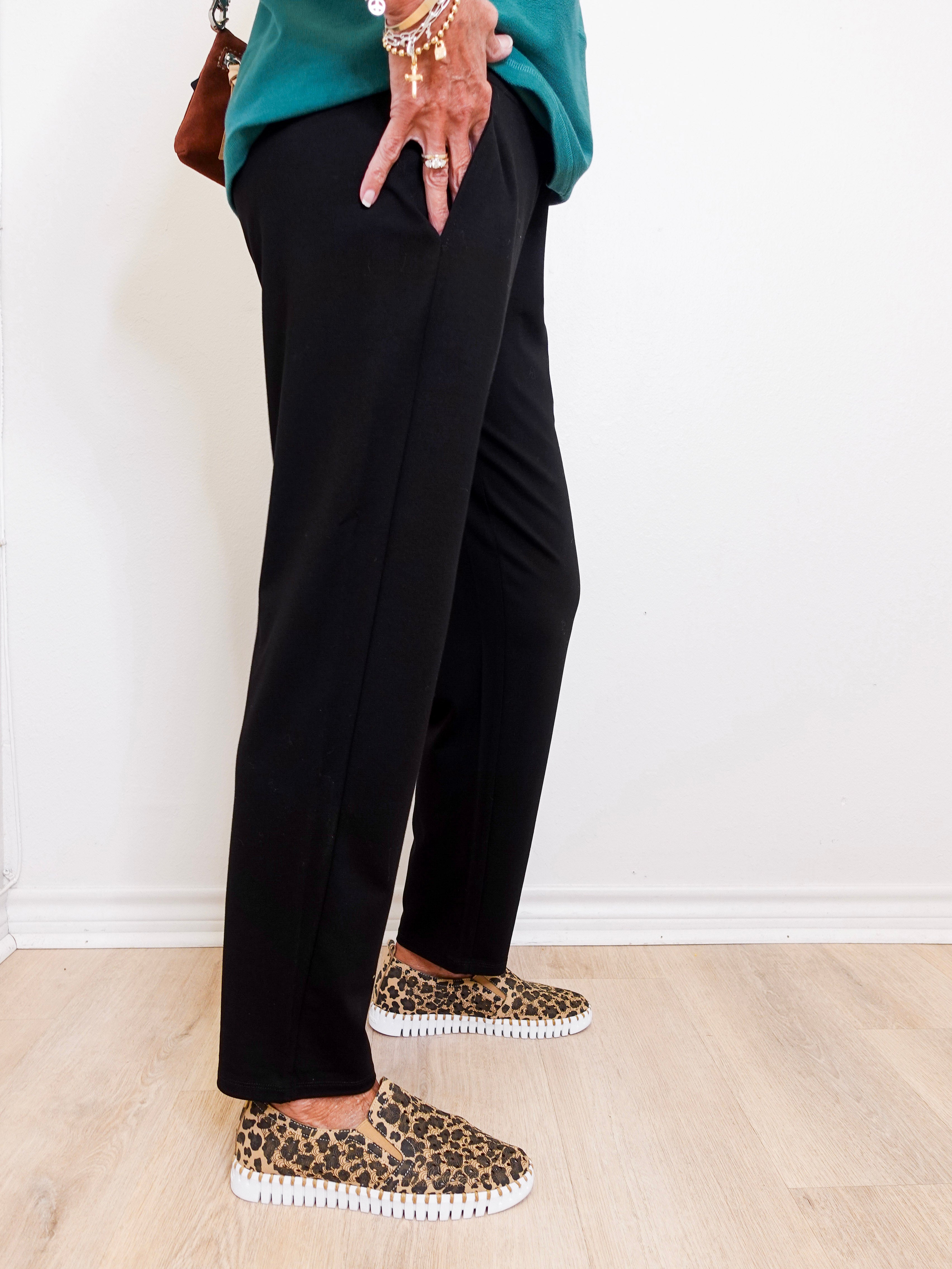 Person wearing black pants and leopard print shoes on a light wooden floor.