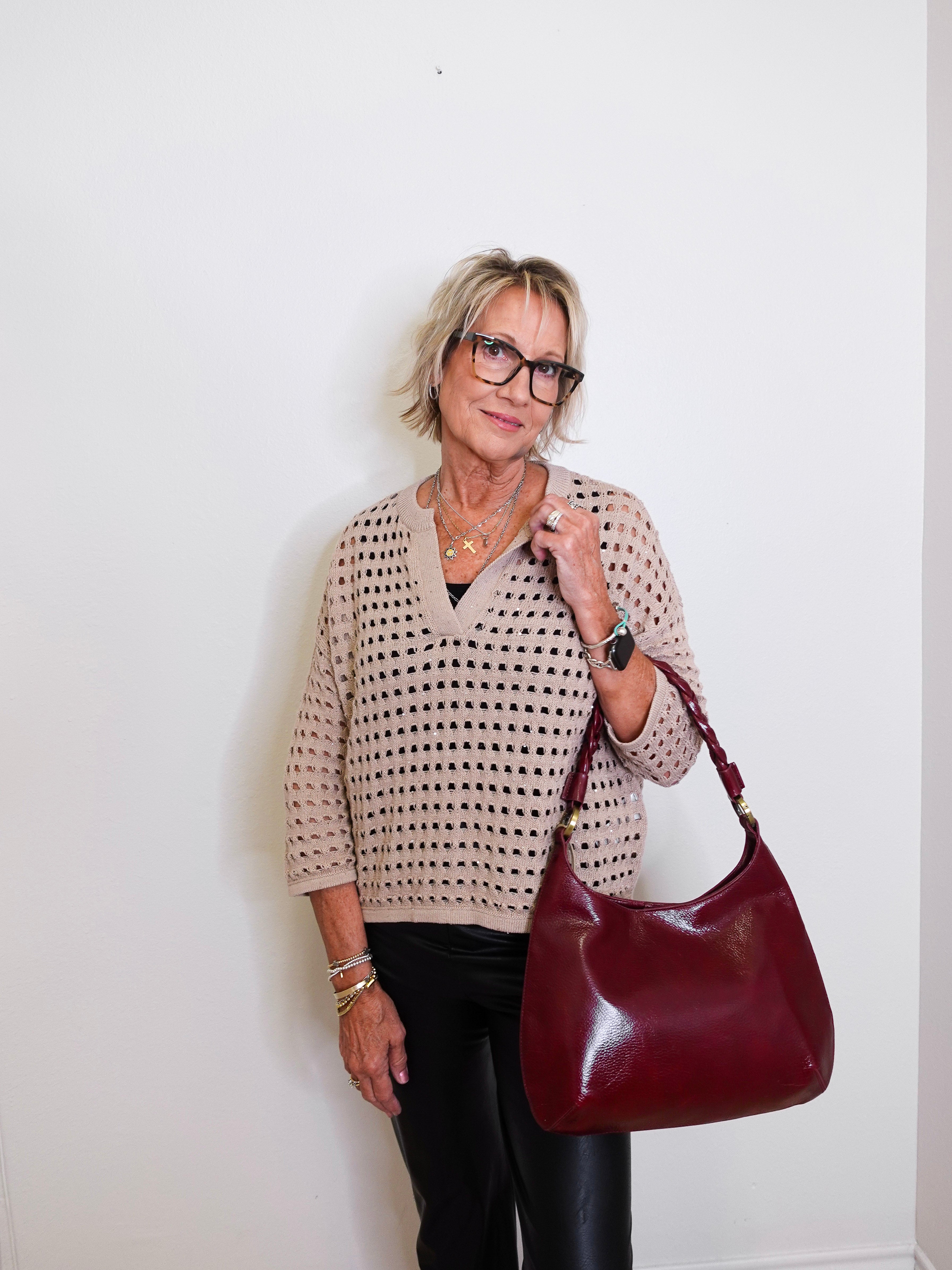 Woman holding a burgundy handbag against a white wall