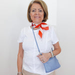 Woman wearing a white blouse with a red scarf and holding a blue handbag against a plain background