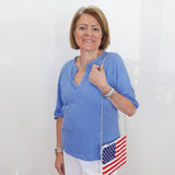 Woman wearing a blue shirt and white pants, holding an American flag bag against a white background