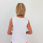 Person wearing a white sleeveless top and red pants against a plain background