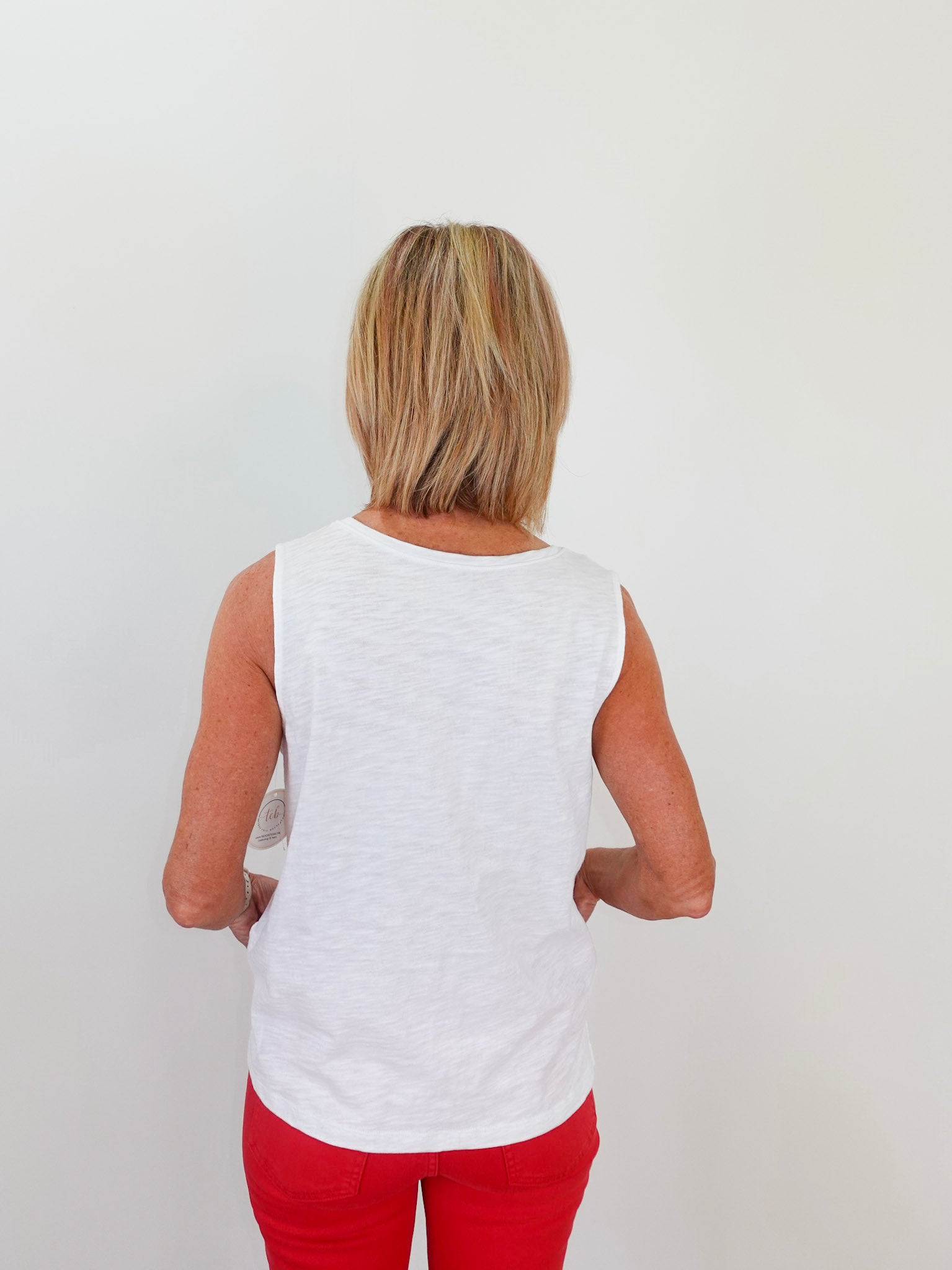 Person wearing a white sleeveless top and red pants against a plain background