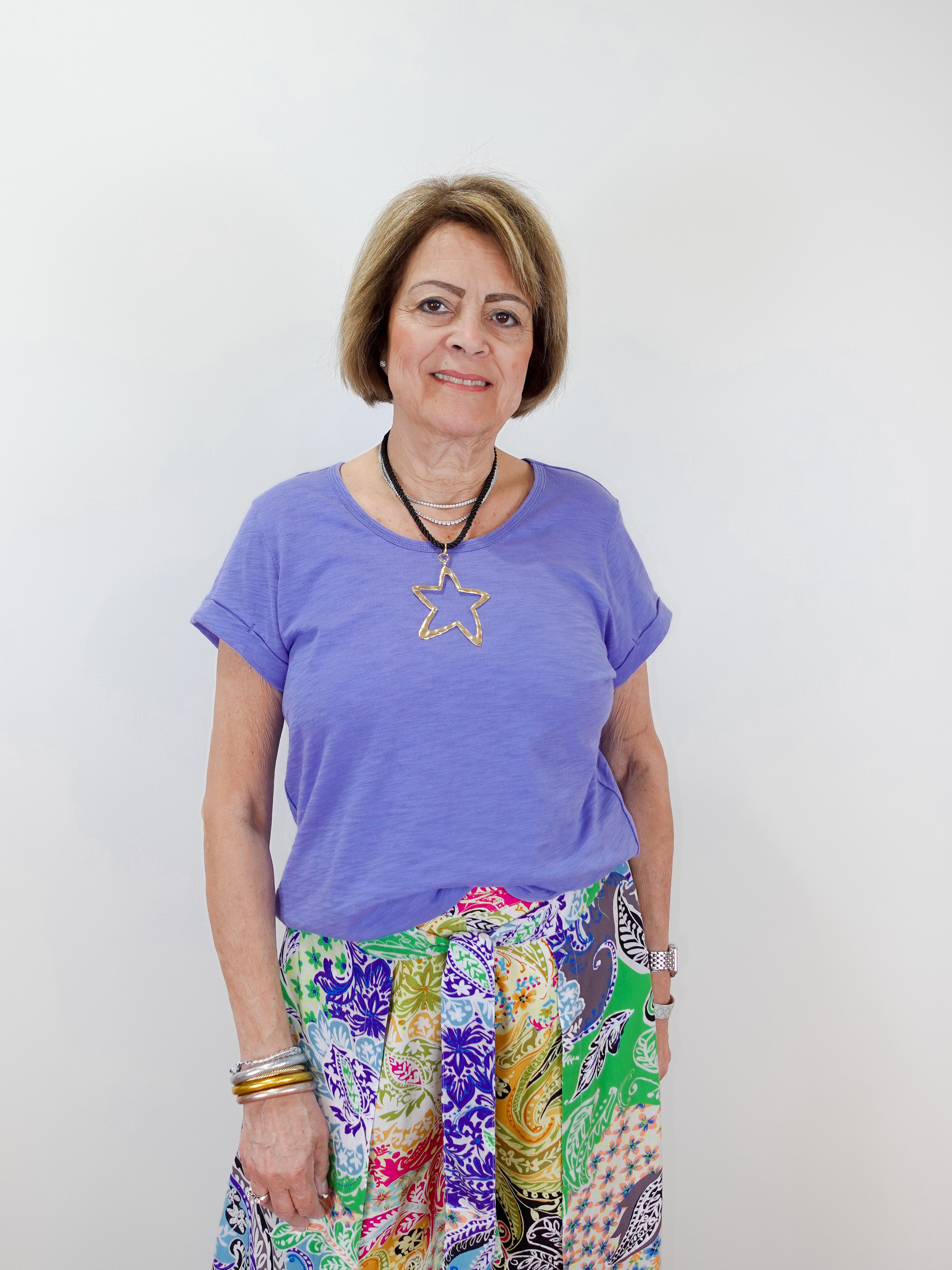 Woman wearing a purple t-shirt with a star design and colorful pants against a white background