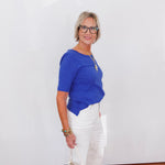 Woman wearing a blue top and white pants against a white background