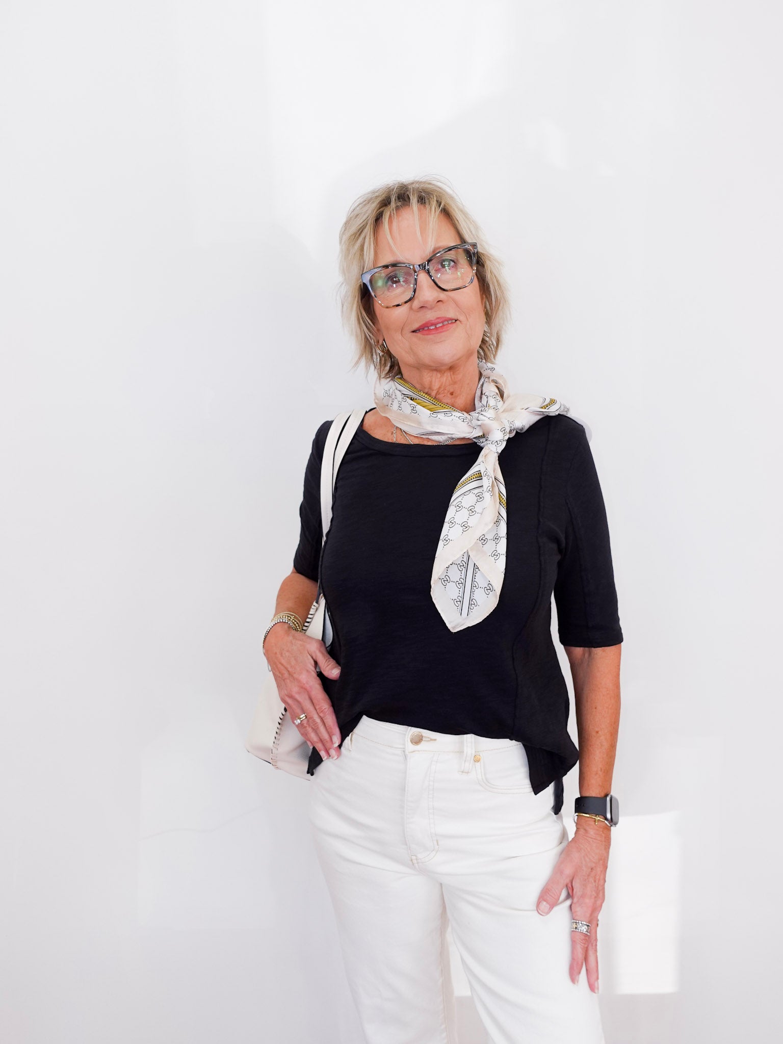 Woman wearing a black top, white pants, and a patterned scarf against a white background