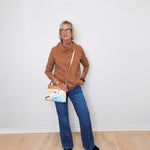 Cozy casual outfit with a tan cowl neck sweater and blue jeans worn by a woman against white background.