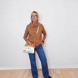 Cozy casual outfit with a tan cowl neck sweater and blue jeans worn by a woman against white background.