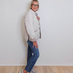 Woman wearing a white quilted jacket and blue jeans against a plain white wall.