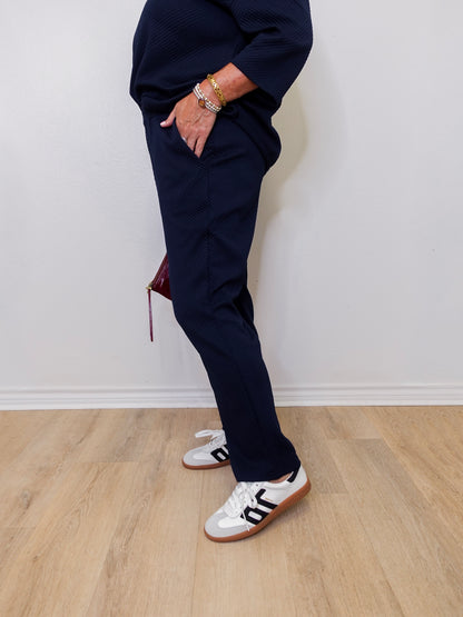 Person wearing navy tracksuit and white sneakers on a light wooden floor.