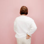 Person wearing a white shirt and beige pants against a pink background