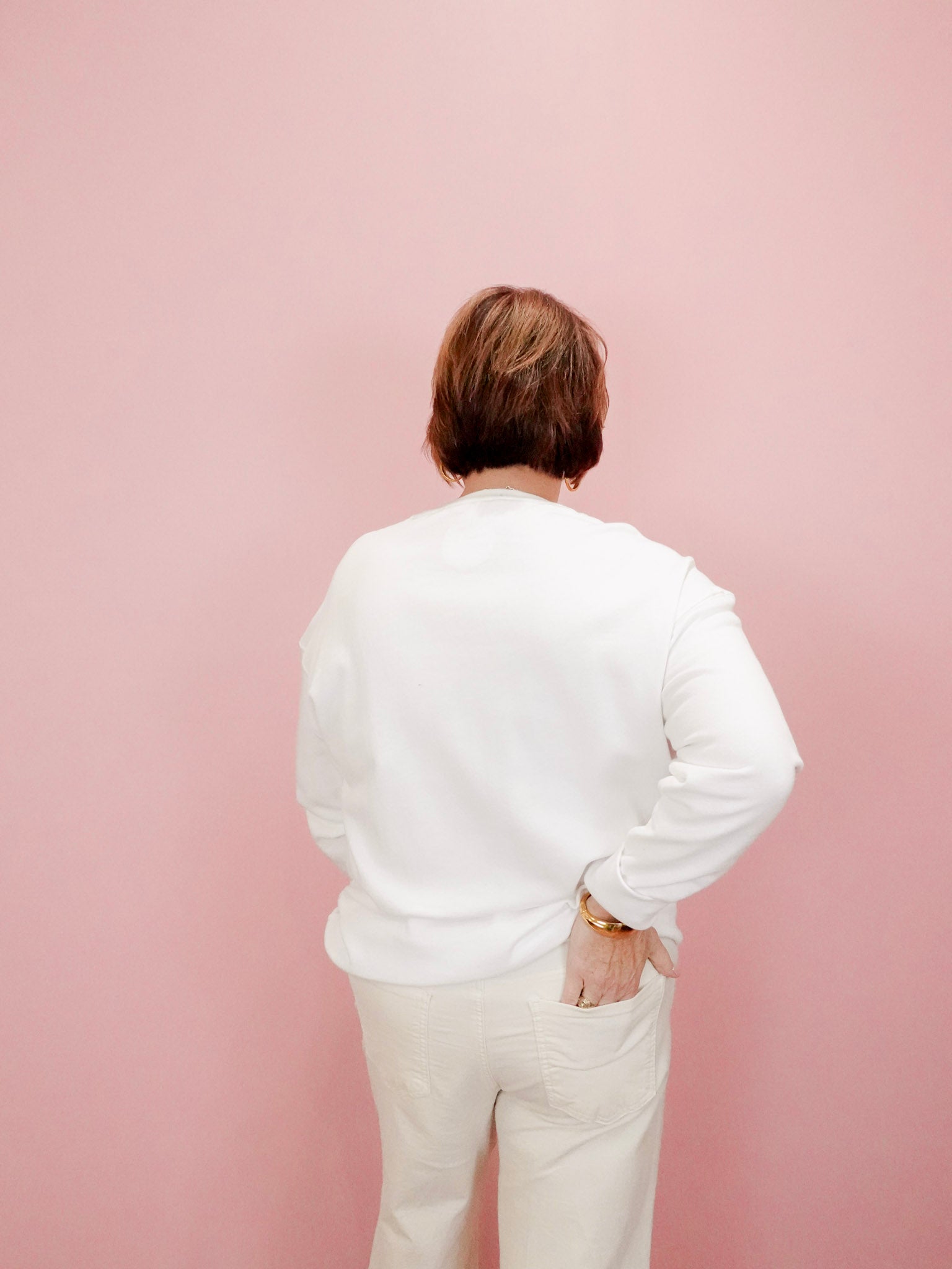 Person wearing a white shirt and beige pants against a pink background